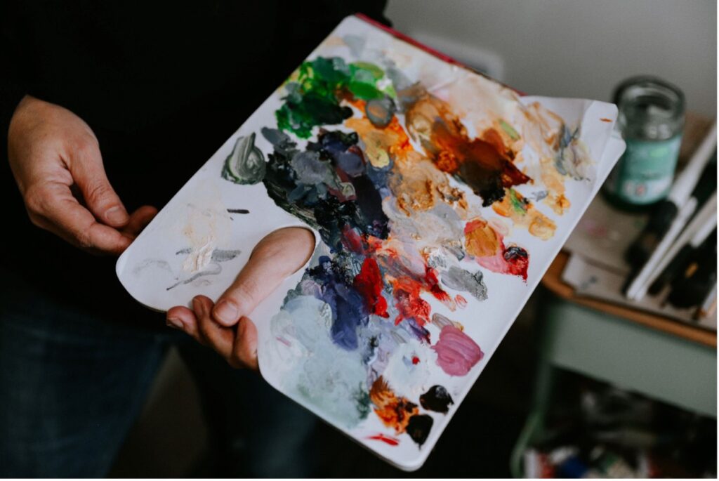 Close-up of hands holding a paint palette smeared with many colours of oil paint